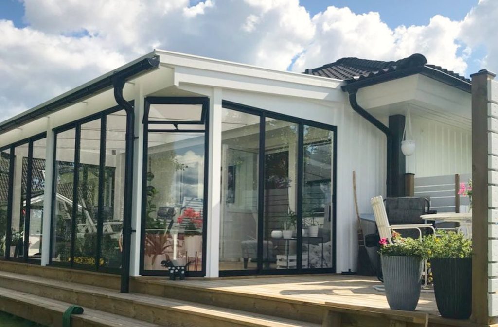 Ett modernt uterum från Expodul Uterum med stora svarta glaspartier och ett pulpettak, anslutet till ett hus.